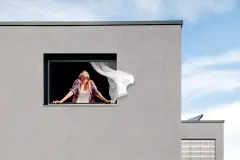Frau steht am offenen Fenster und atmet ein