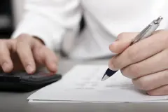 Eine Person mit Taschenrechner und Stift stellt eine Rechnung auf.