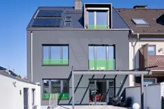 Haus mit großflächiger dunkelgrauer Putzfassade und grünen Glaselementen
