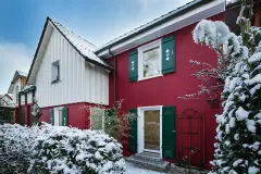 Haus mit roter Putzfassade, weißer Holzfassade und grünen Fensterläden