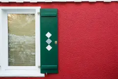 Rote Putzfassade mit grünen Fensterläden