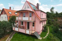 Haus mit rosaroter Putzfassade und Holzterrasse.