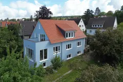 Hellblaues Einfamilienhaus mit Satteldach und kubischem Anbau. Vogelperspektive.