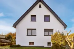 Frontalansicht eines Einfamilienhauses, die Sonne lässt die cremefarbene Fassade erstrahlen