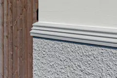 Detailansicht einer Fassade mit Gesims, Strukturputz und Holz