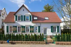 Wohnhaus mit weißer Fassade, grünen Fensterläden und Gesims an den Fenstern