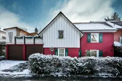 Haus mit roter Putzfassade, weißer Holzfassade und grünen Fensterläden