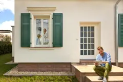 Frontalansicht eines Hauses mit grünen Fensterläden und Gesims über den Fenstern.