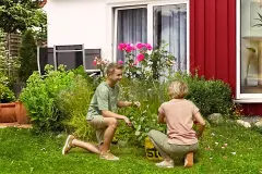 Mutter und Sohn arbeiten im Garten hinter dem Haus mit roter Holzfassade