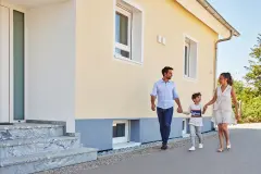 Familie läuft unbeschwert am Haus entlang zum Eingang
