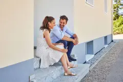 Mieter-Paar sitzt fröhlich auf der Treppe vor dem Haus